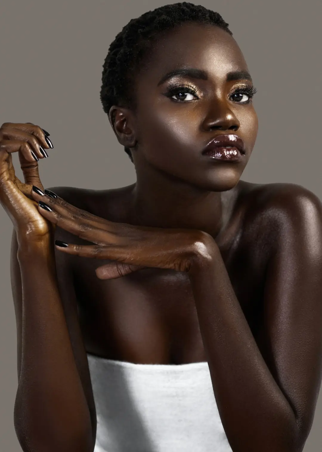 Close-up beauty editorial photograph highlighting luminous dark skin, glossy lips and expressive hands