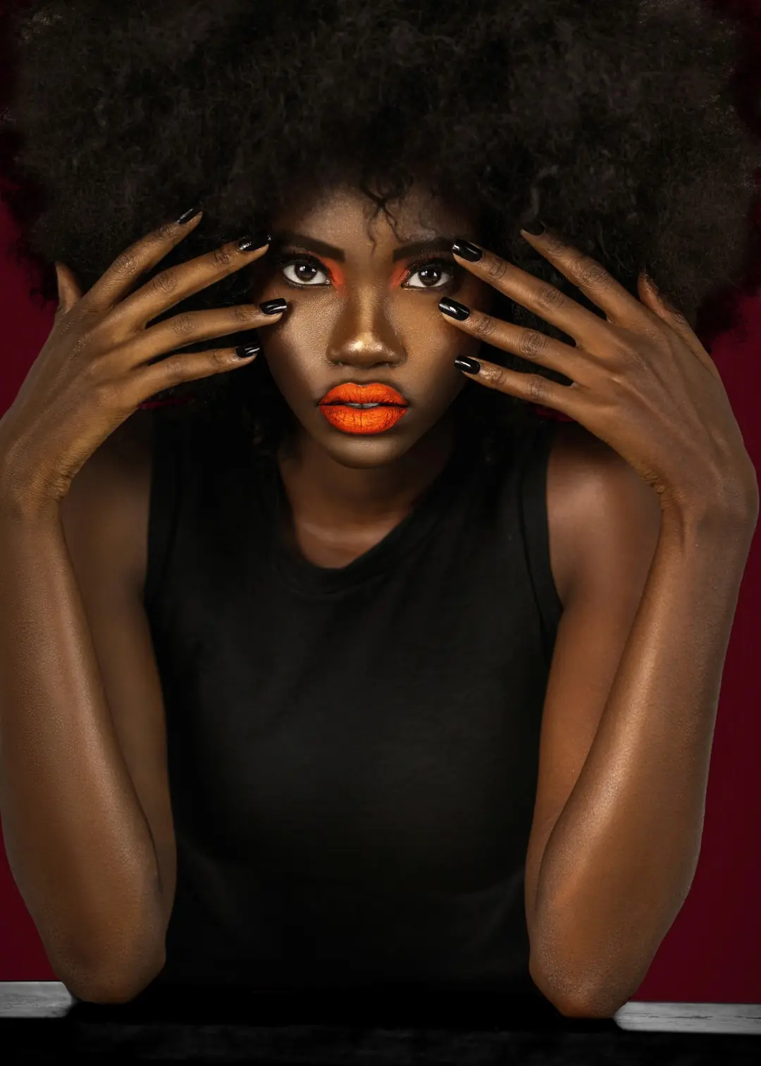 Beauty editorial portrait with orange makeup, natural textured hair and sculptural hand placement