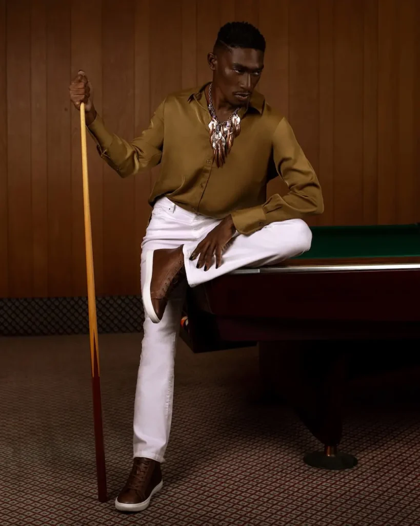 Male model seated beside a pool table in a full-length vertical fashion portrait