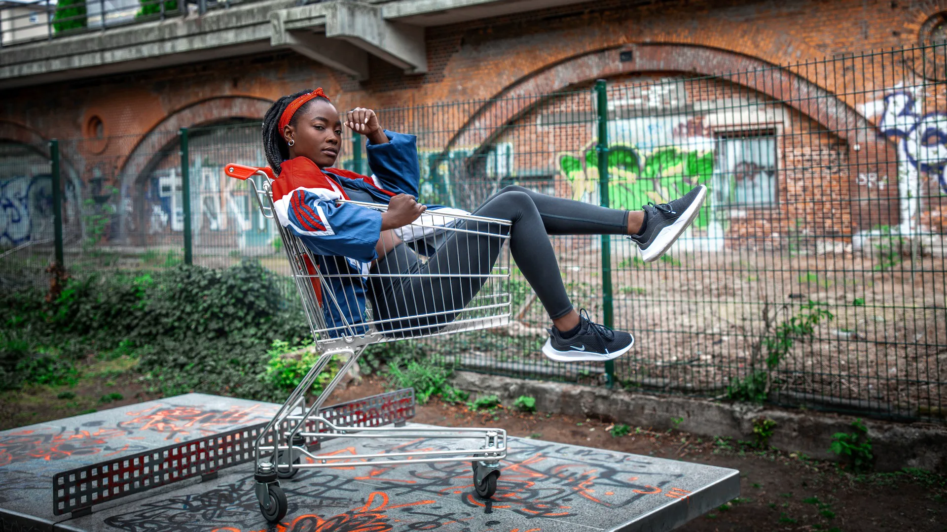 Female athlete seated in a shopping cart beside a graffiti-covered Berlin court