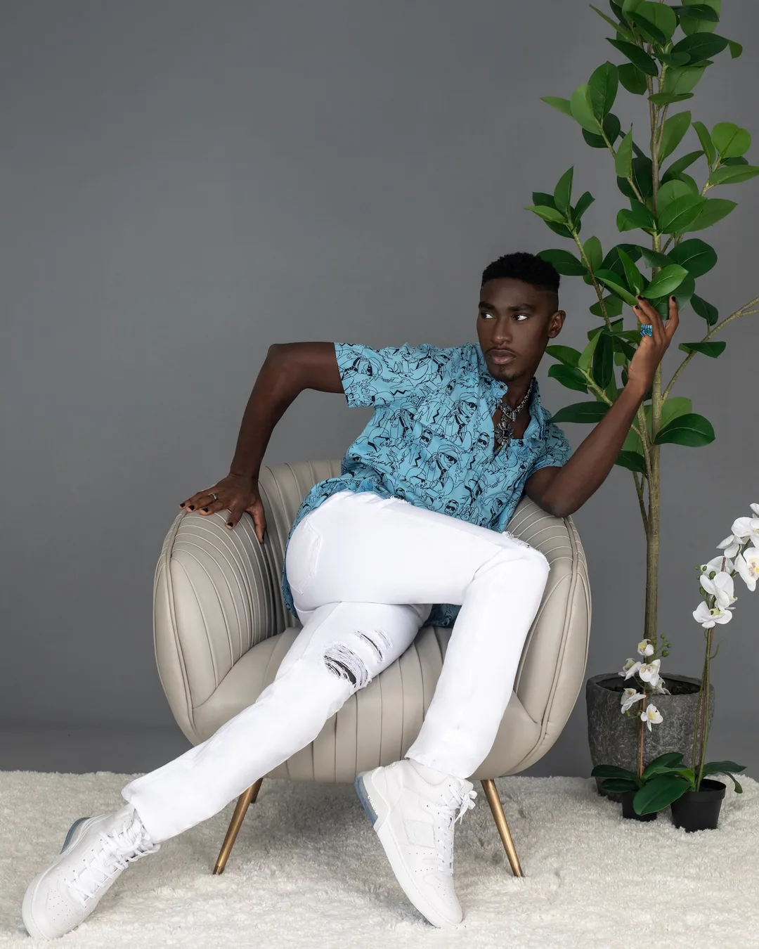 Troy seated in a blue printed shirt and white trousers