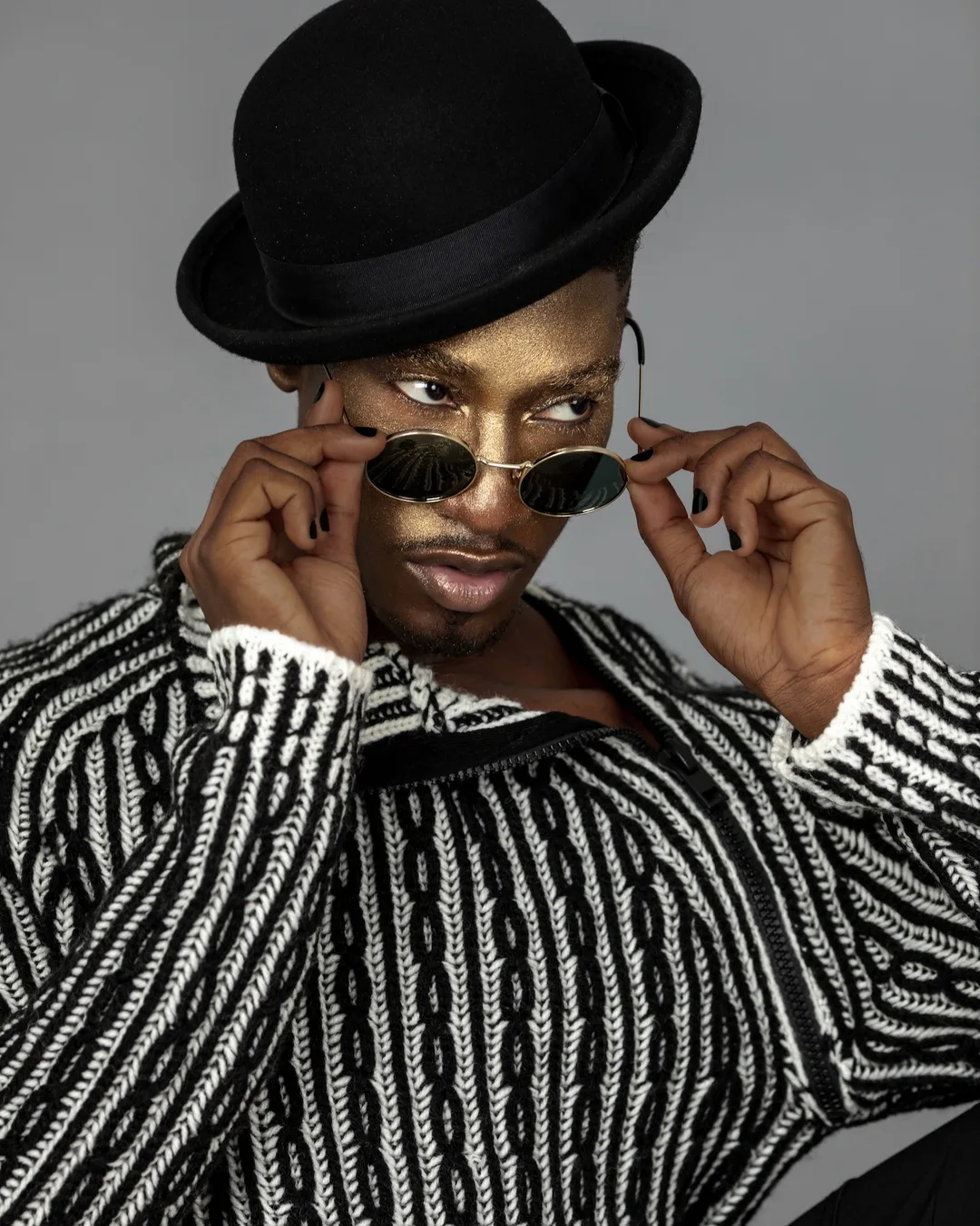 Close-up of Troy wearing a black hat, sunglasses, gold makeup and black nail polish