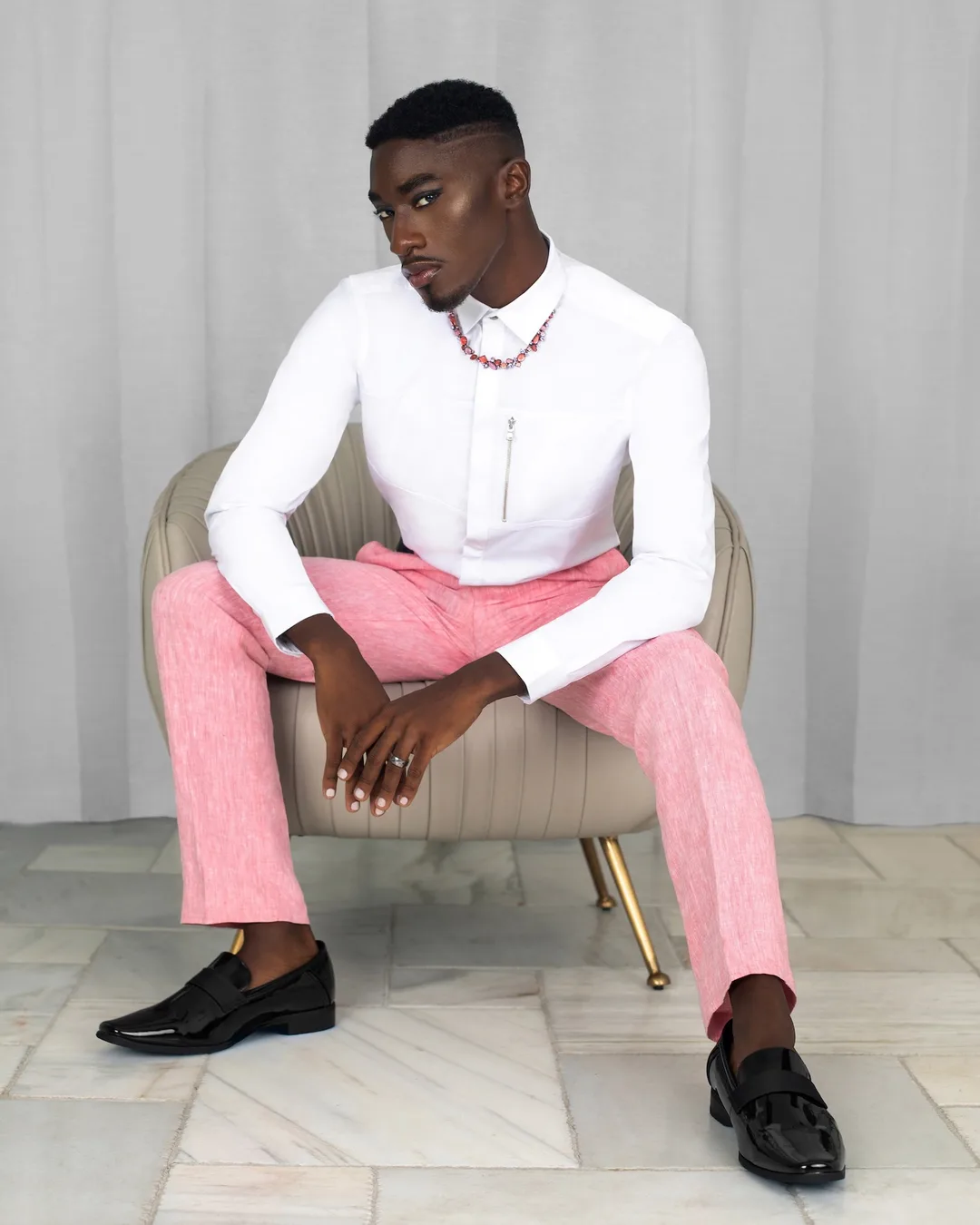 Troy seated in a white shirt and pink trousers for the Pretty Boy Joy fashion editorial