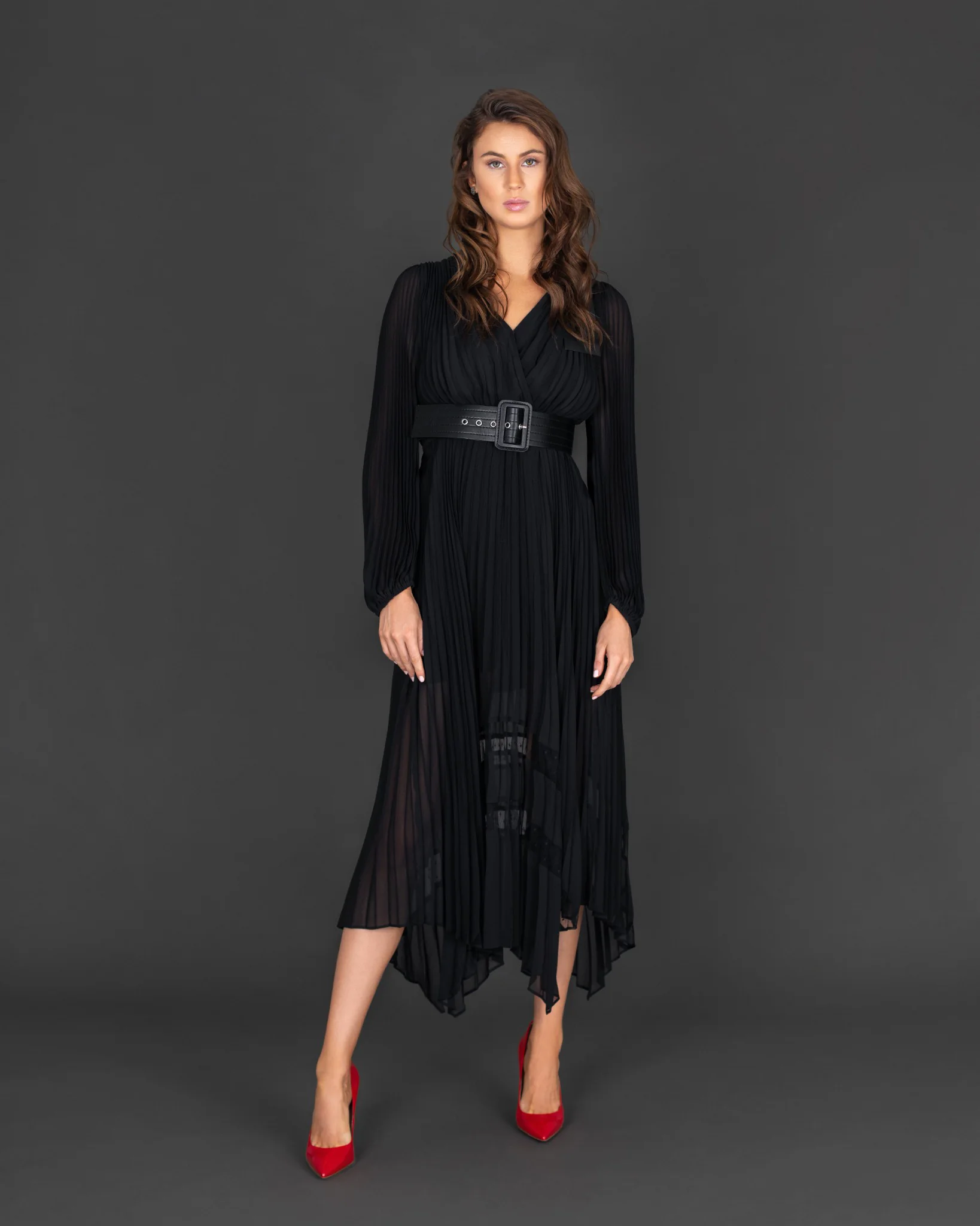 Full-length studio portrait of Rebecca wearing a pleated black dress and red heels