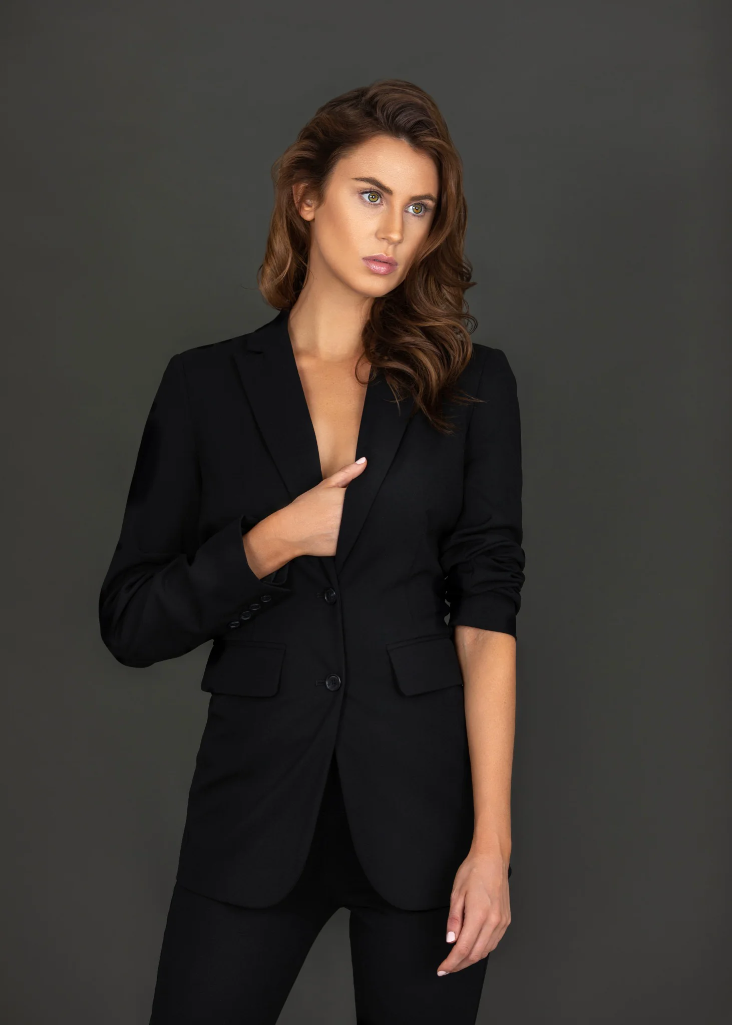 Model Rebecca standing in a black tailored suit for a vertical studio fashion portrait