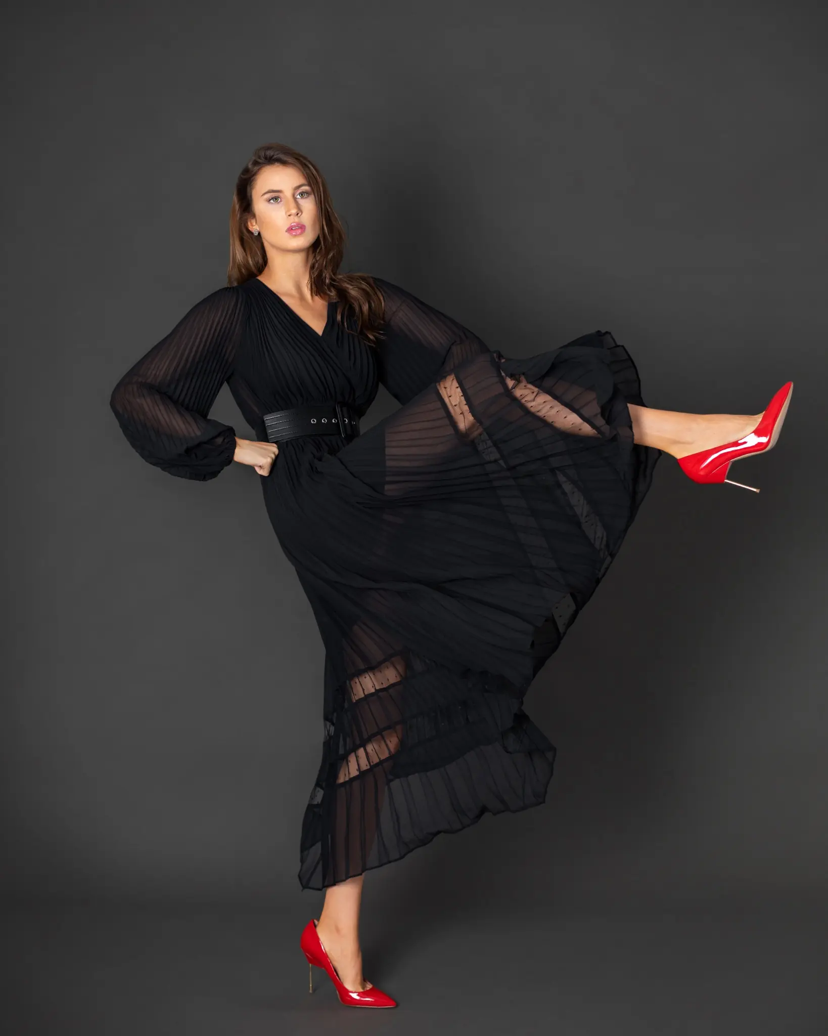 Rebecca creating movement in a black pleated dress with red heels during a studio fashion shoot