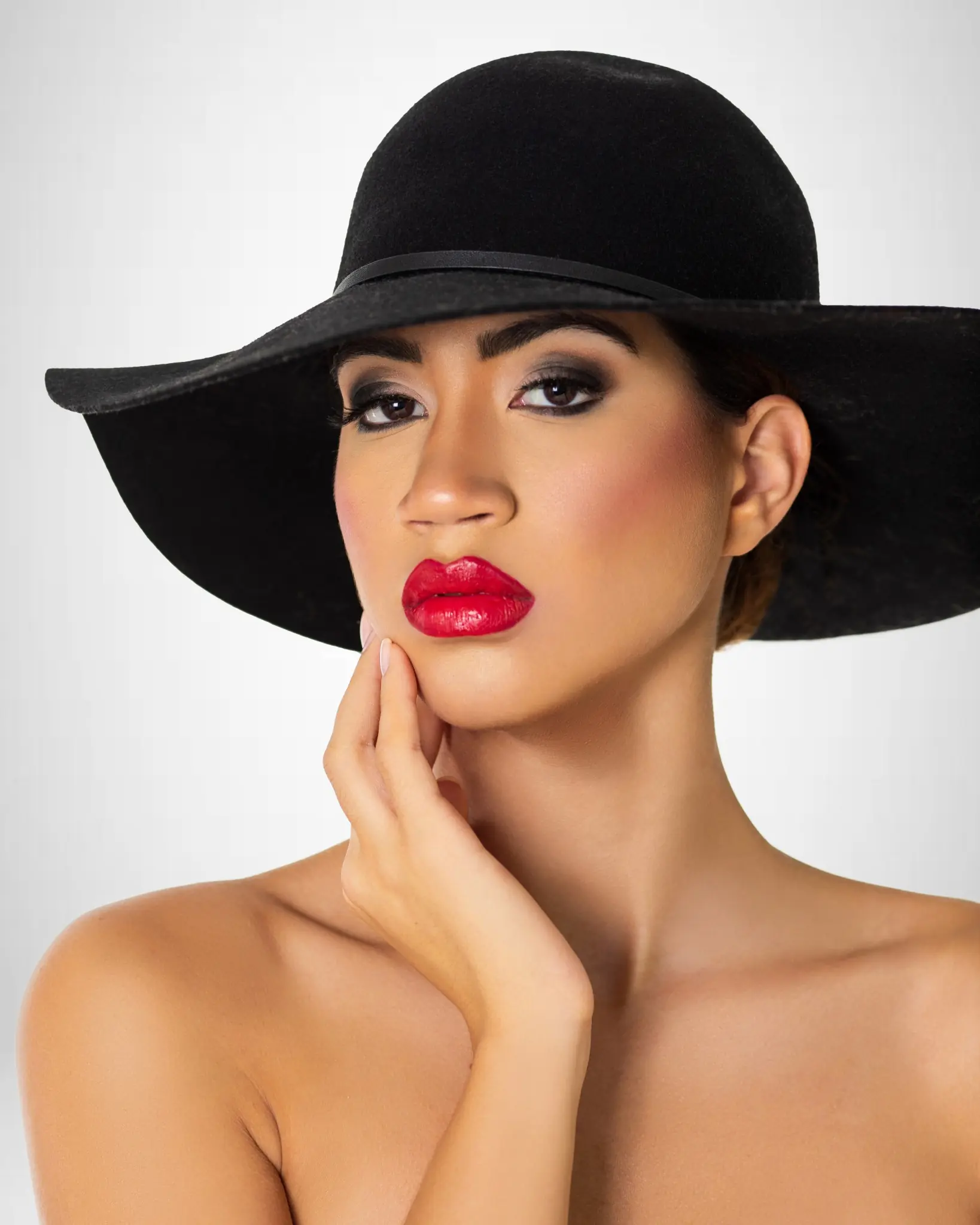 Close-up beauty portrait of Sangella wearing a wide black hat with smoky eye makeup and red lipstick