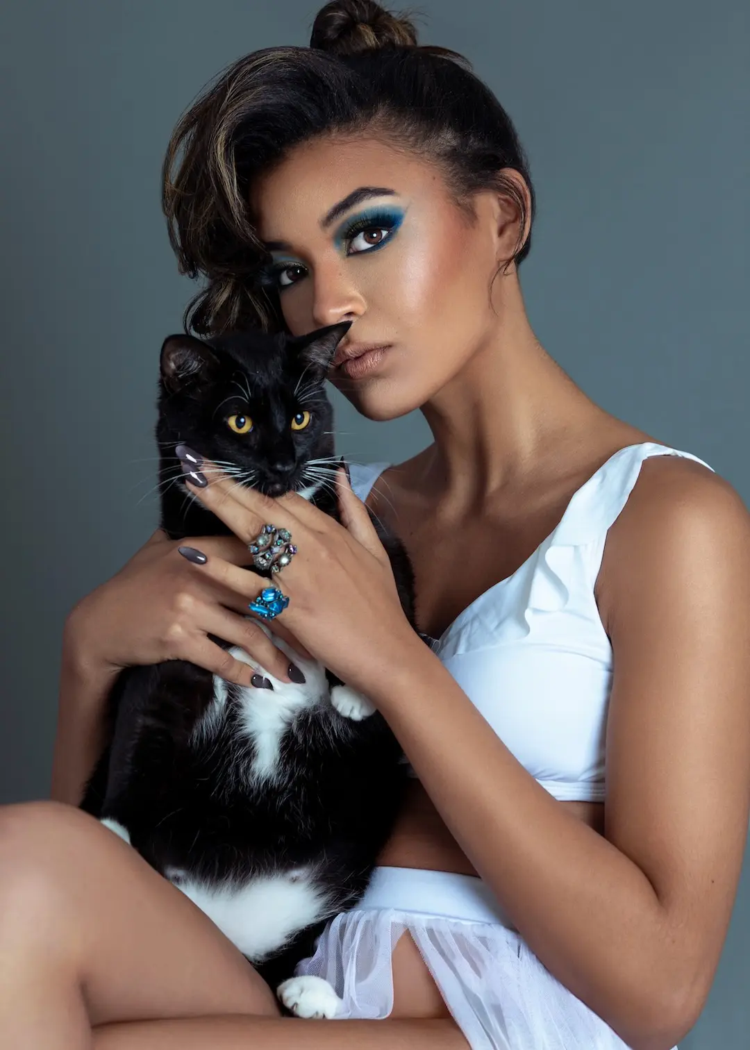 Fianna holding a black cat while wearing blue eye makeup and statement jewelry.