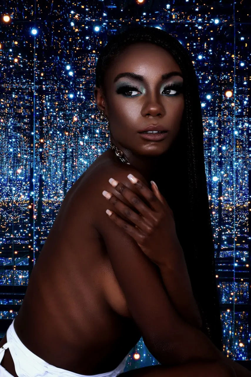 Bare-shoulder beauty portrait with blue eye makeup against a reflective blue background