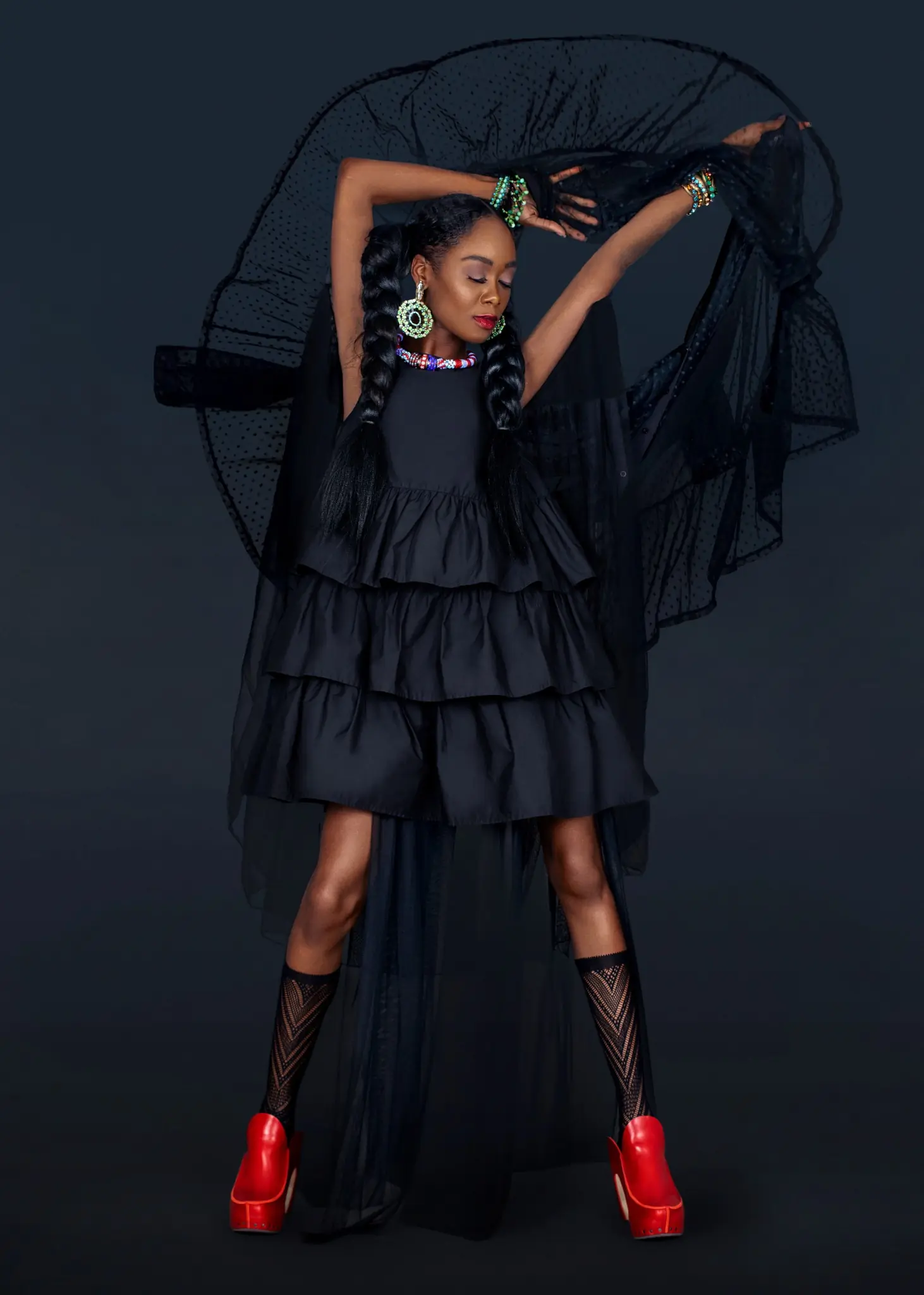 Maria posing beneath an arc of black tulle in a black dress and vivid red shoes