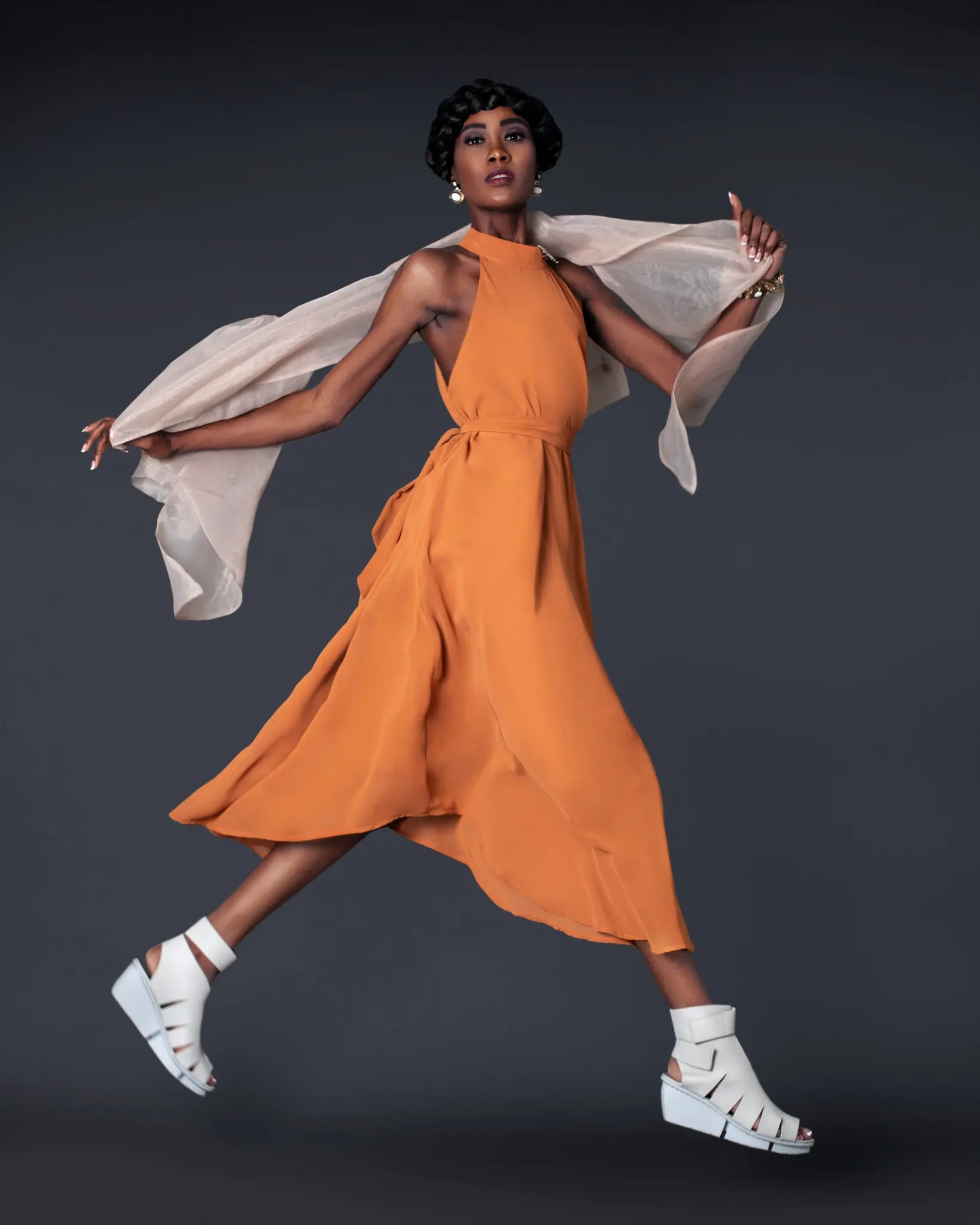 Maria moving through the studio in a flowing burnt-orange maxi dress and white platform sandals