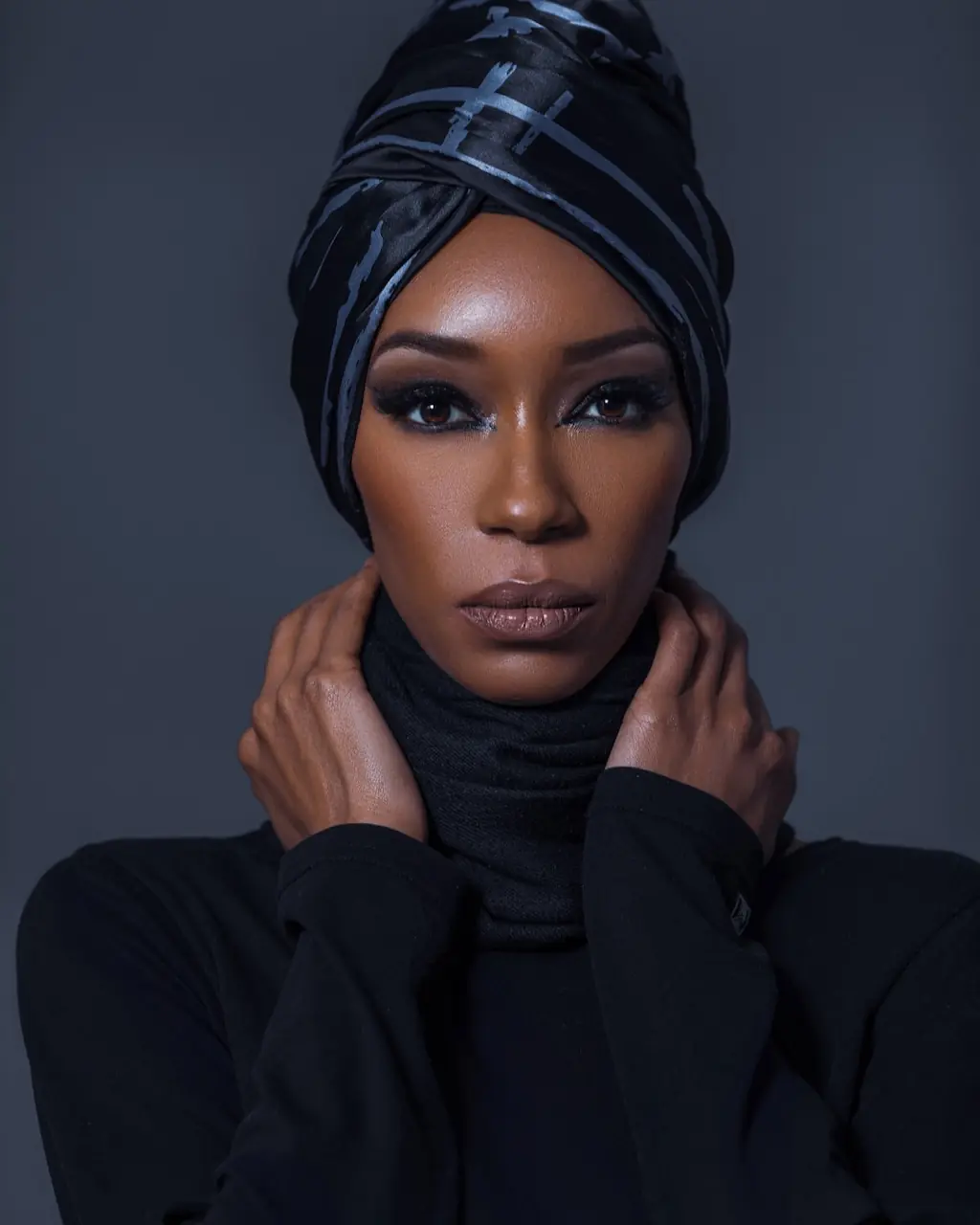 Studio Fashion Editorial Production: Simple Comforts - Phil Halfmann Front-facing beauty portrait of Jovona Logan in a black headwrap with her hands at the wrapped neckline.