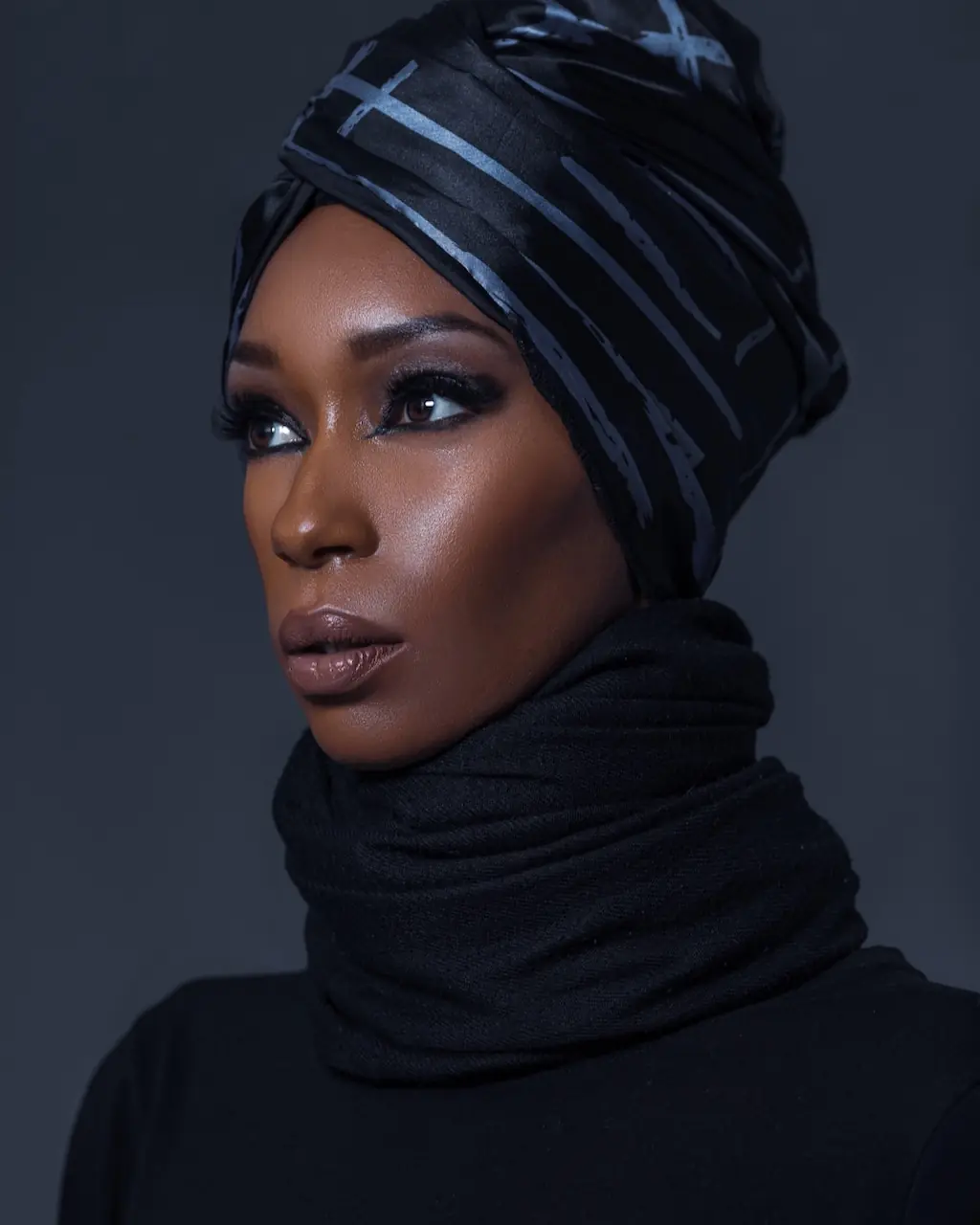 Studio Fashion Editorial Production: Simple Comforts - Phil Halfmann Side-facing beauty portrait of Jovona Logan in a patterned black headwrap and wrapped black neckline.