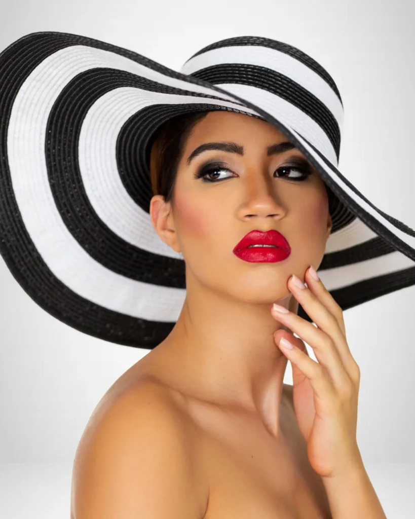 Close-up fashion beauty portrait of Sangella wearing a wide black-and-white striped hat and vivid red lipstick